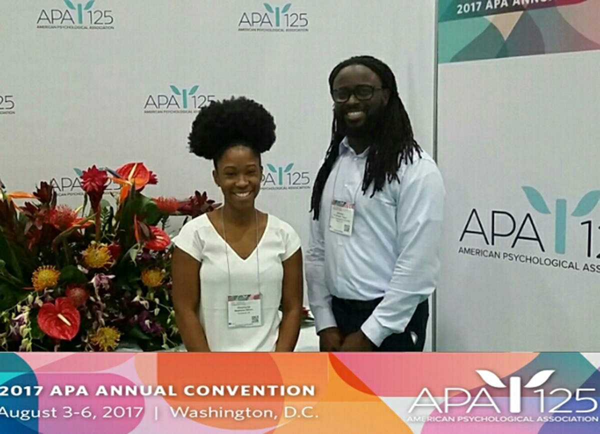 Stephanie and Alfonso pose at the 2017 APA Convention, which was August 3-6 in Washington, D.C. A large urn of flowers is placed nearby.