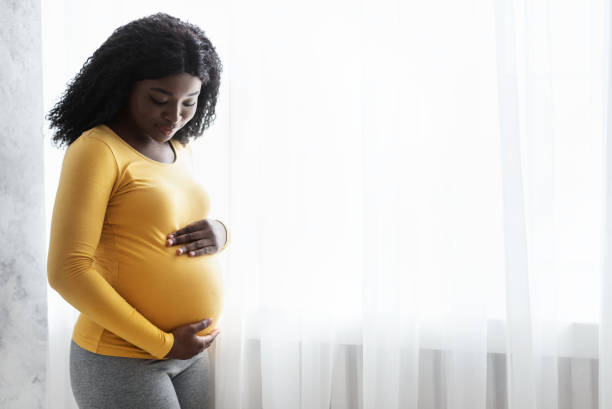 Black woman in yellow shirt holding her baby bump.